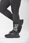 Person wearing black athletic shoes and leggings with 'Women Hustle Harder' text on a white background