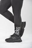 Person wearing black athletic shoes and leggings with 'Women Hustle Harder' text on a white background